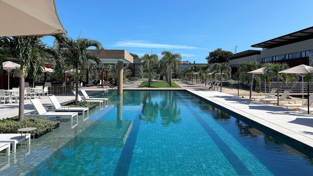 A swimming pool with lounge chairs and umbrellas, surrounded by palm trees and modern buildings. - Flat Ilê de Pipa Tulum - By Almare (Tibau do Sul)