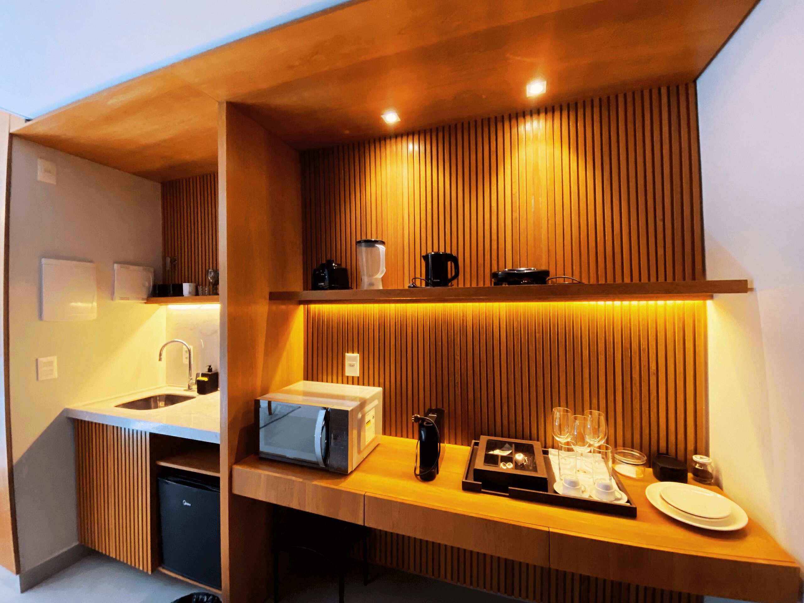 A compact kitchen with a microwave, kettle, and coffee maker on the counter, and a sink with a faucet.