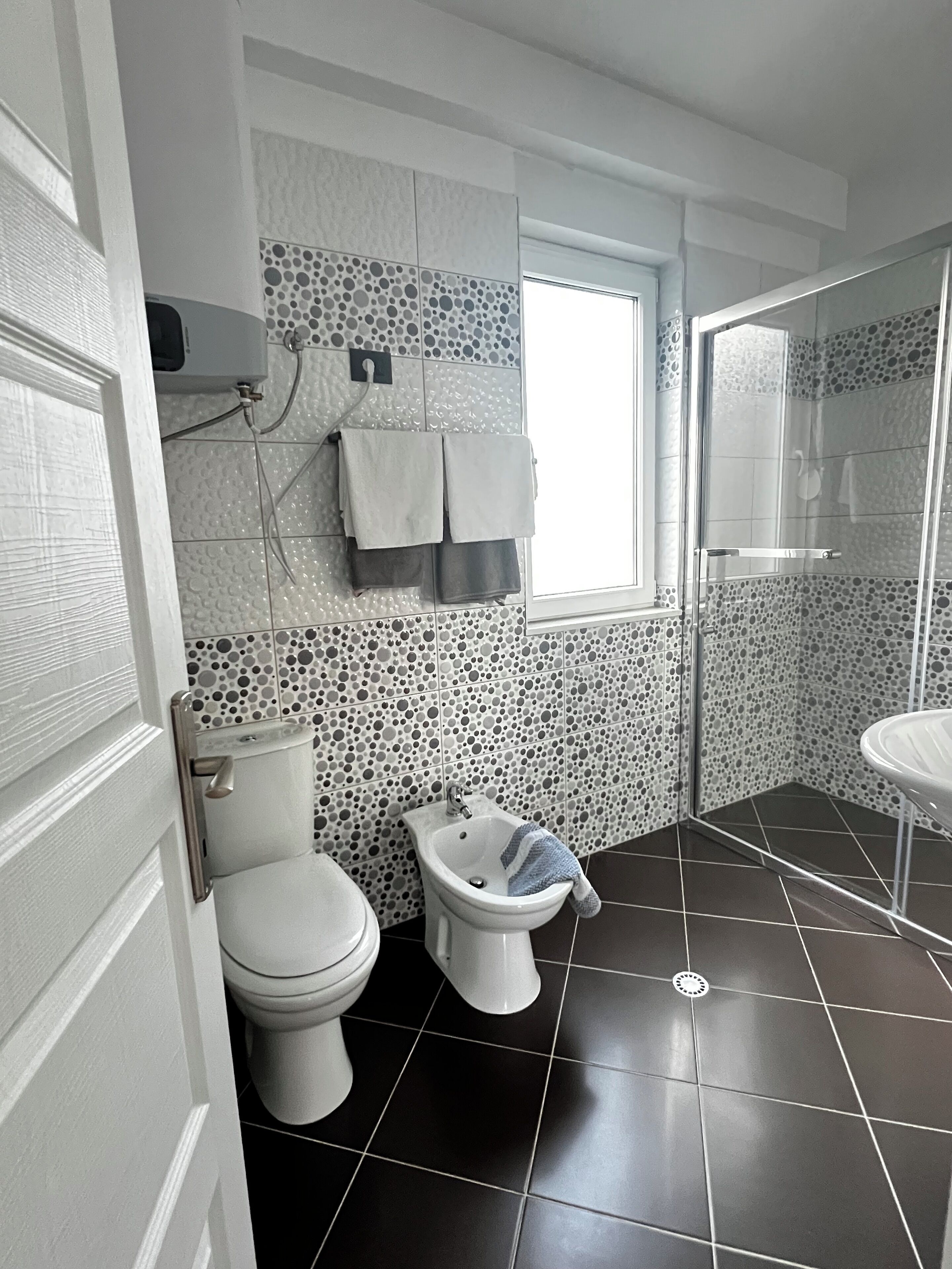A bathroom with a toilet, bidet, and sink, tiled with a polka dot pattern.