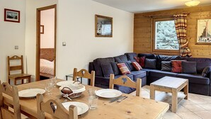 Ein gemütliches Zimmer mit einem Holzesstisch für zwei Personen, einem dunkelblauen Sofa und einem Fenster mit Blick auf Bäume.