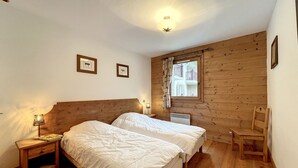 Ein Schlafzimmer mit einem hölzernen Kopfende, zwei Betten, einem Nachttisch, einem Sessel und einem Fenster mit Blick auf einen Balkon.