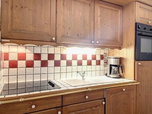 Una cocina con gabinetes de madera, salpicadero de azulejos, estufa, lavabo y cafetera.