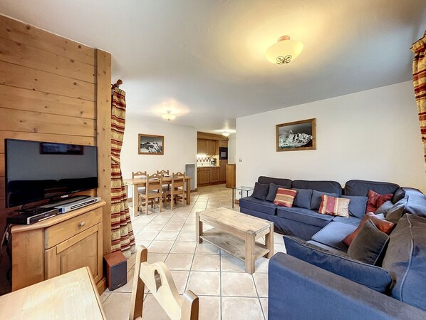 Una sala de estar con televisor, muebles de madera, un sofá y un comedor con mesa y sillas.