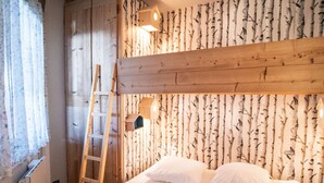 Una habitación con una cama litera, paredes de madera, una escalera y una lámpara fijada a la pared.