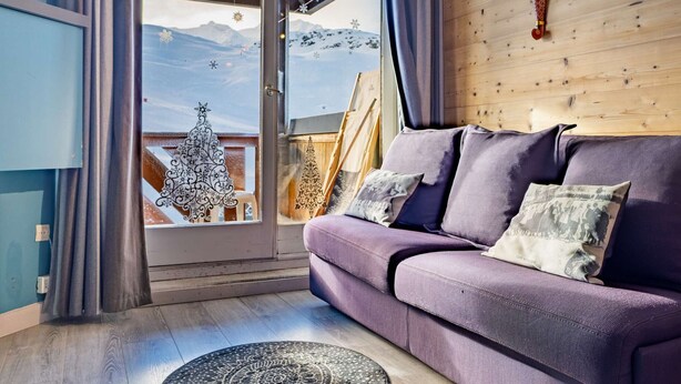 Una sala de estar con un sofá morado, una pared de madera y vistas a montañas a través de un ventanal.
