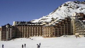 Un hotel grande con varios pisos, pistas de esquí y una montaña cubierta de nieve al fondo.