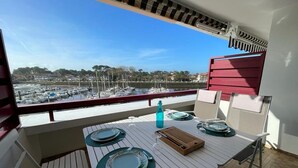 Ein Balkon mit Esstisch, Blick auf einen Yachthafen mit Booten und Gebäuden in der Ferne.