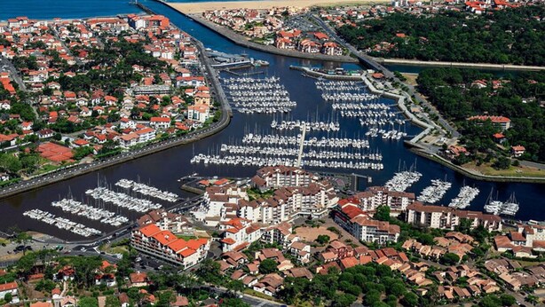 Eine Luftaufnahme einer Küstenstadt mit einem Hafen voller Boote, umgeben von Wohnhäusern mit roten Dächern.