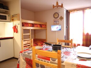 Una cocina compacta con una cama litera, un microondas y un televisor.