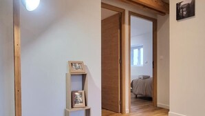 Un corridoio con pavimento in legno, una mensola di legno con cornici e una porta che conduce a una camera da letto con un letto.