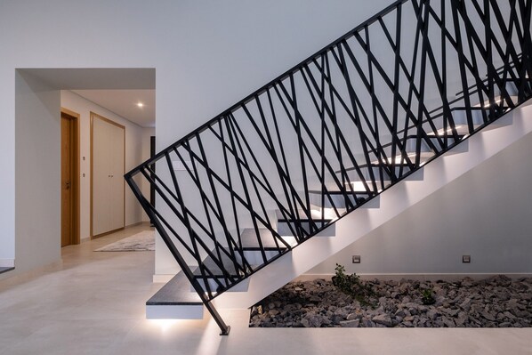 A modern staircase with a black metal railing, a wooden door, and a stone accent wall. - Casa da Suta - Jacuzzi com Vista mar (Ribeira Grande)
