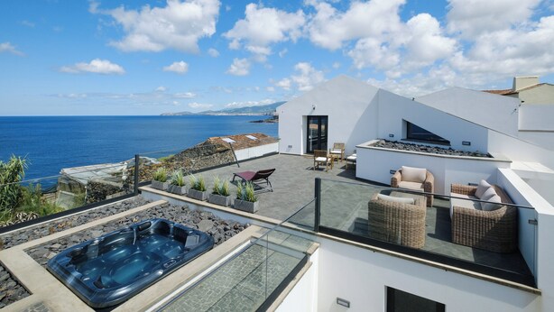 Una terraza moderna en la azotea con jacuzzi, mobiliario exterior y vistas al mar.