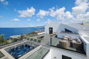 A modern rooftop with a hot tub, outdoor seating, and a view of the sea. - Casa da Suta - Jacuzzi com Vista mar (Ribeira Grande)