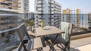 Un balcon avec une table et des chaises, donnant sur un paysage urbain avec des bâtiments modernes.