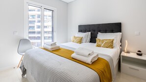 Une chambre d’hôtel moderne avec un grand lit, une table de chevet, une chaise et une fenêtre donnant sur la ville.