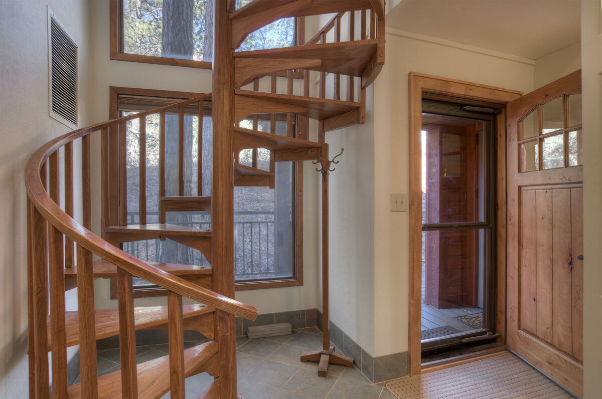 Un escalier en colimaçon en bois se trouve dans une pièce dotée de grandes fenêtres et d’une porte donnant sur l’extérieur.