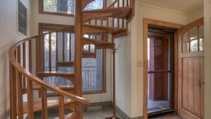 Una escalera en espiral de madera en una habitación con ventanas grandes y una puerta que da al exterior.