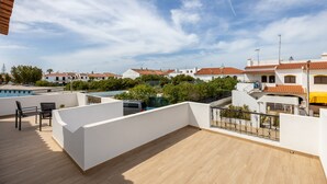 Une terrasse sur le toit, dotée d’un plancher en bois, de murs blancs et offrant une vue sur les maisons voisines.