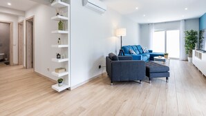 Un salon moderne avec un canapé gris, un canapé bleu et une étagère blanche agrémentée de plantes.