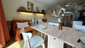 A dining area with a wooden table set for two, white chairs, a vase with flowers, and a painting on the wall.