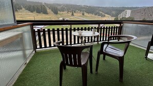 A balcony with a view of a forested landscape and a distant building.