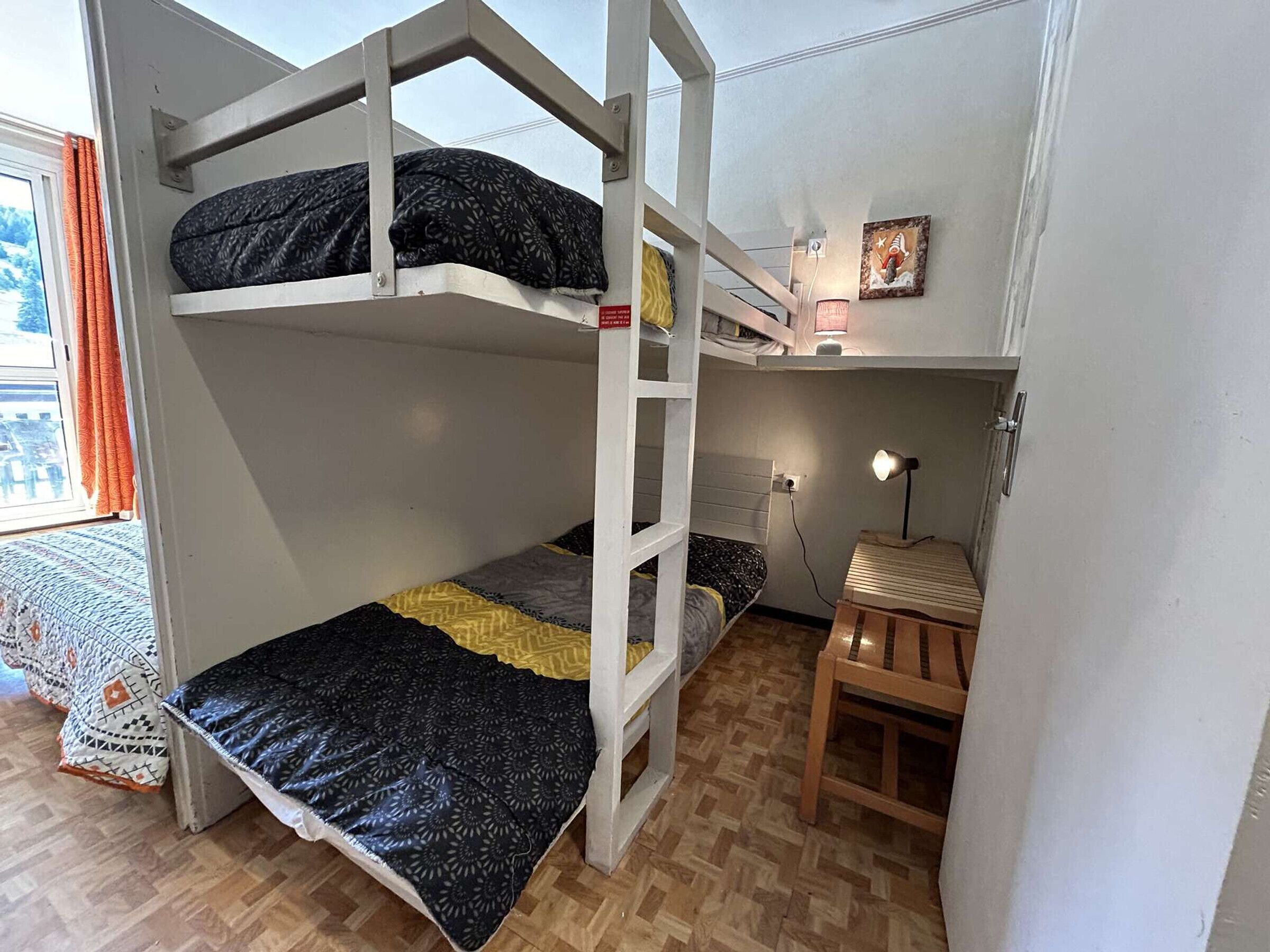 Habitación con literas, una escalera de madera, un escritorio con lámpara y una ventana con cortinas.