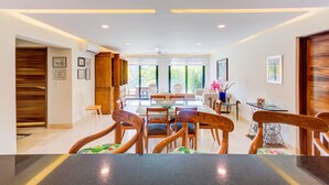 Un vaste espace dédié à la salle à manger, avec une longue table et des chaises, un coin cuisine doté de meubles en bois, et une vue sur l’extérieur grâce à de grandes fenêtres.