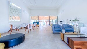 Un vaste espace de vie au design moderne, comprenant différents types de sièges, notamment des canapés et des fauteuils, une table basse et une vue dégagée grâce à de grandes fenêtres.