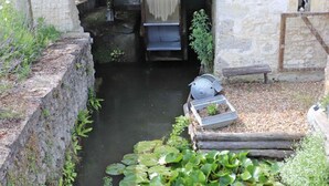 Un stretto canale navigabile con una panchina in legno e un piccolo giardino con piante e una ruota idraulica.