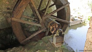 Un'antica ruota idraulica con meccanismo metallico, inserita in una struttura in pietra vicino all'acqua.