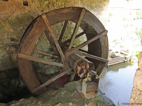 An old water wheel with a metal mechanism, set in a stone structure near a body of water.