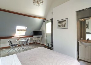 Een slaapkamer met een bed, een bureau met een computer, een stoel, een raam en een badkamer met een wastafel en spiegel.