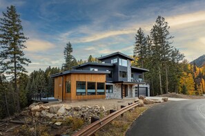 A modern two-story house with a wooden exterior and large windows, surrounded by a forest and mountains. - New Lake Front Home Across from Purgatory - Multiple Decks, Views & Ping Pong (Durango)