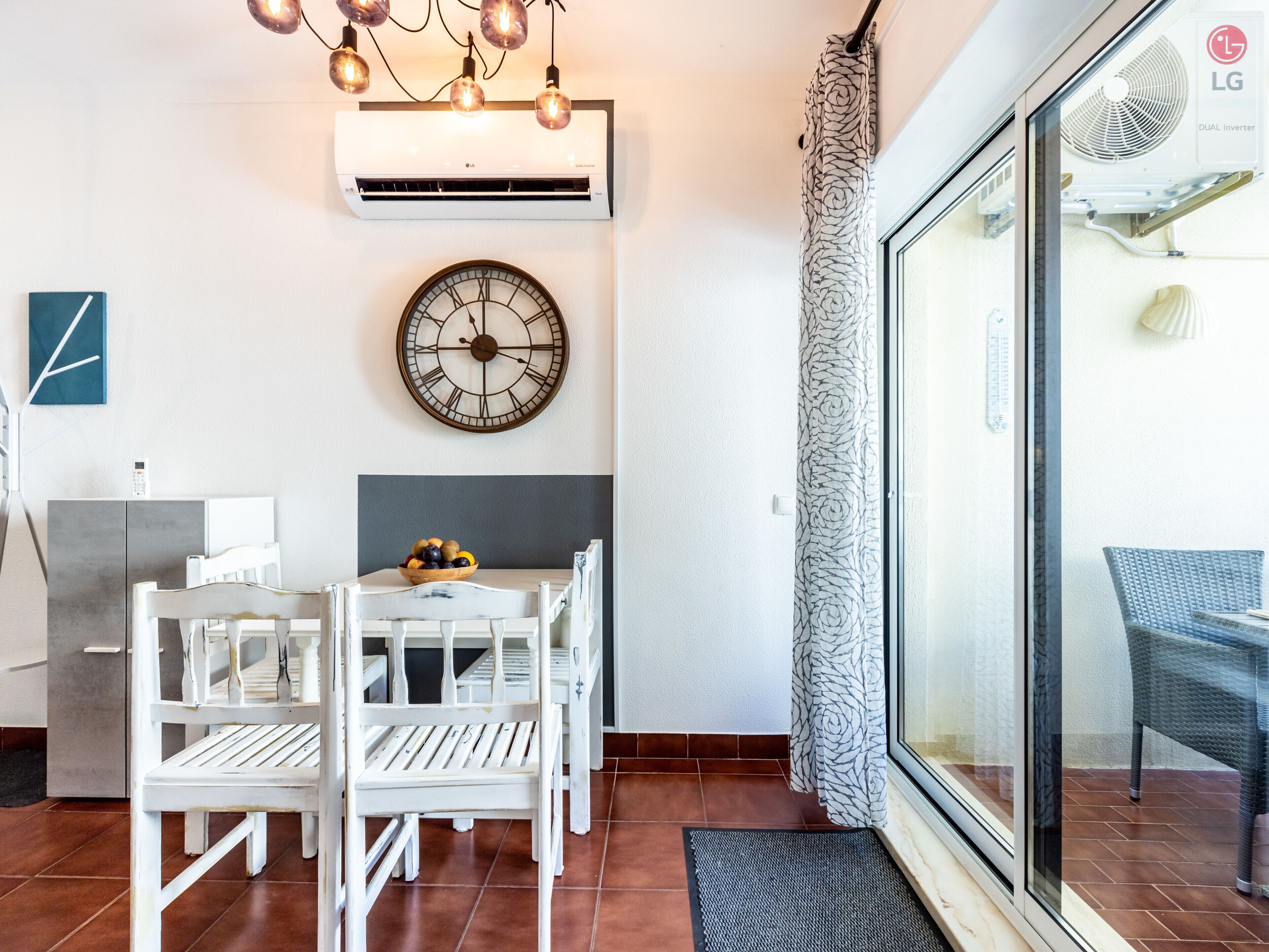 Uma sala de jantar com uma mesa branca, cadeiras e um relógio na parede.