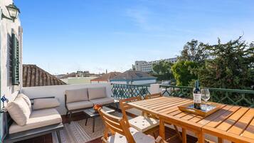 Una terraza en la azotea con una mesa de madera, sillas, un sofá y vistas panorámicas de la ciudad.