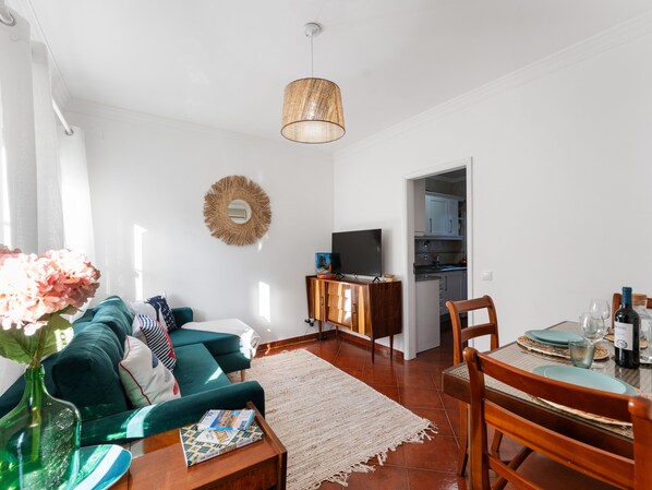 A living room with a sofa, a coffee table, a TV, and a dining area with chairs and a table.