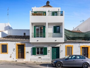 A two-story building with green shutters, a balcony, and a car parked in front.