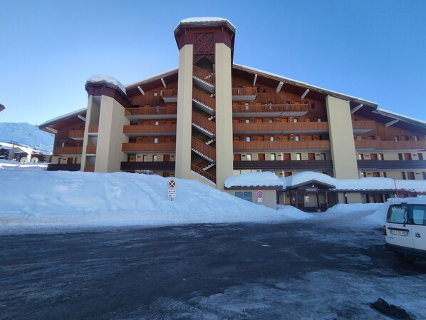 Un hôtel à plusieurs étages, doté d’une tour centrale, de balcons et d’un parking enneigé.