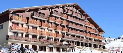 A multi-story hotel with balconies and a ski slope in the background.