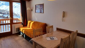 A cozy room with a wooden table and chairs, a sofa, a window with a view of snow-covered mountains, and a mounted telephone.