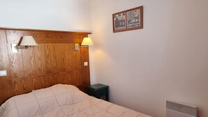 A bedroom with a wooden headboard, a bed with a quilt, a nightstand, a wall-mounted lamp, and a radiator.