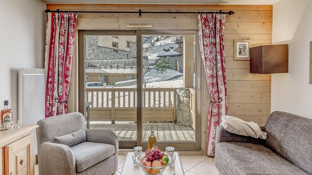 A cozy living room with a wooden table, two sofas, and a view of a snowy balcony.