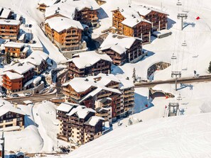 Un centro turístico nevado en la montaña con varias edificaciones de madera, telesillas y cielo despejado.