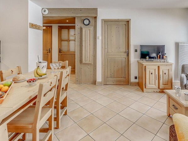 A cozy kitchen with wooden furniture, a dining table set with fruits and glasses, a TV, and a cabinet with a mirror. - Tignes - Premium Apartment 6 ppl, balcony, parking included (Tignes)