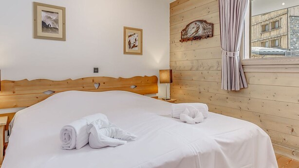 A neatly made bed with white linens and towels, a wooden headboard, and a wooden wall with a sign. - Tignes - Premium Apartment 6 ppl, balcony, parking included (Tignes)