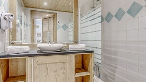 Un baño con tocador de madera, un lavabo blanco y zona de ducha.
