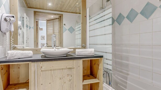 Une salle de bain avec un meuble-lavabo en bois, un lavabo blanc et un espace douche.