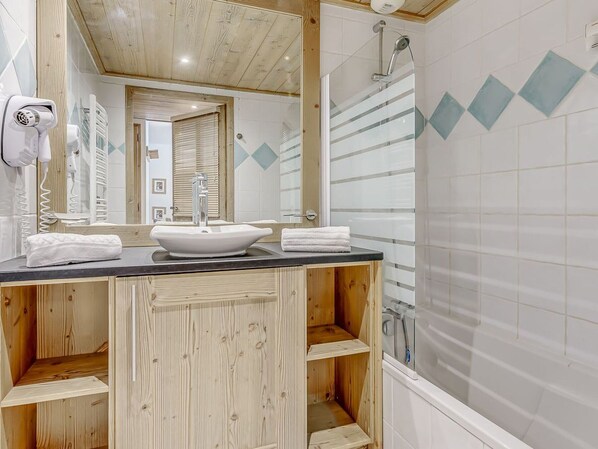 A bathroom with a wooden vanity, a white sink, and a shower area.