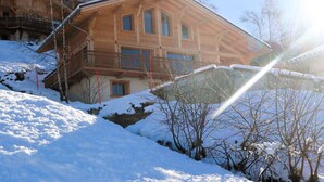 A wooden chalet with balconies, set on a snowy hillside.