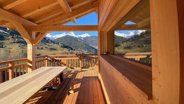 A wooden deck with a table and benches, overlooking a mountainous landscape.